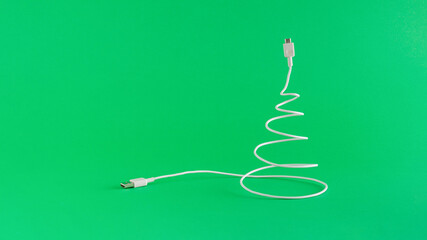 Creative digital Christmas arrangement made of USB cable in the shape of a Christmas tree. on a vivid green background. Minimal New Year concept with copy space. Online holiday inspiration.