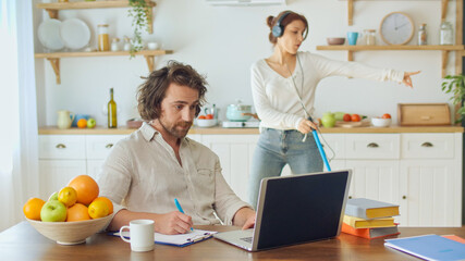Attractive Man Trying to Work Remotely While His Wife With Headphones Dancing and Singing Karaoke...