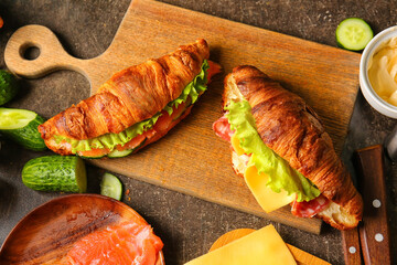 Wooden board with tasty croissant sandwiches on table