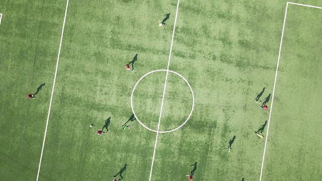 Aerial view of soccer players playing football on green sports stadium.