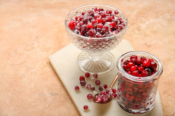 Glass bowl and jar with tasty sugared cranberries on beige background