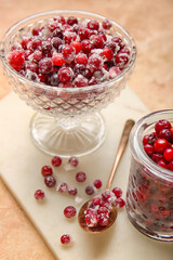 Glass bowl and jar with tasty sugared cranberries on beige background