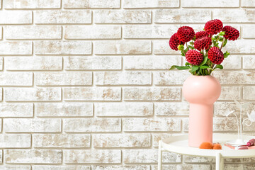 Vase with beautiful dahlia flowers on table near brick wall, closeup