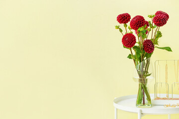 Vase with beautiful dahlias and female accessories on table against color background, closeup