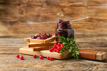 Jar of tasty lingonberry jam and toasts on wooden background