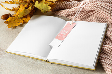 Blank open book with bookmark and oak leaves on light background