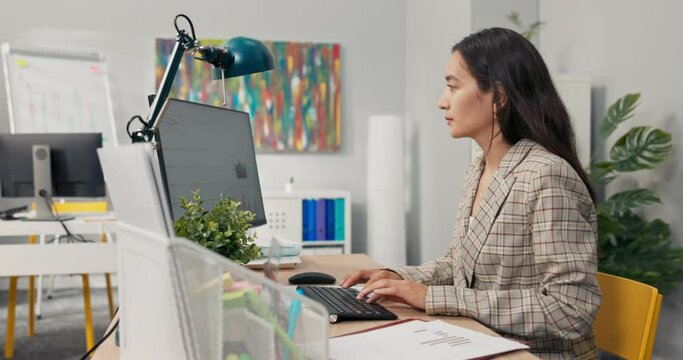 An attractive, experienced company accountant sits in office in front of a computer checking statistical data employee salary charts comparing paper diagrams with electronic ones financial analyst