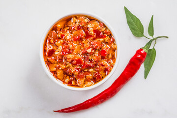 Chili red hot pepper sauce in oil  and fresh chili pepper on white marble background copy space.