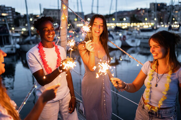 Group of people having fun and celebrating new year night with sparklers on a boat - Happy lifestyle concept - Focus on african man