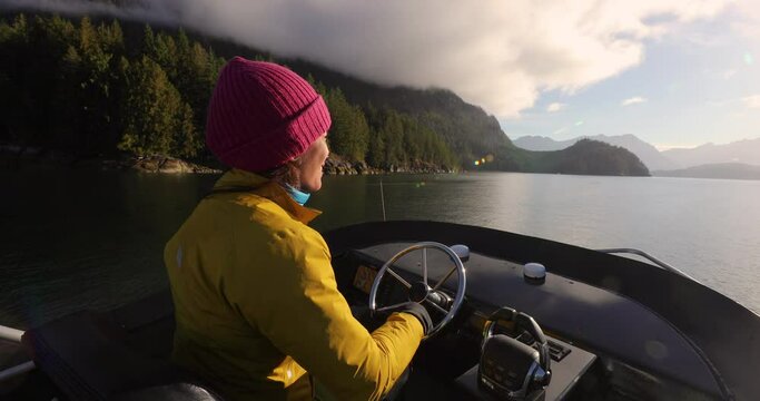 Woman Driving Motor Boat in Beautiful Nature Landscape Smiling Happy at Sunset in Coastal British Columbia Near Bute, Toba Inlet, and Campbell River. Whale Watching Tourist Travel Destination, Canada