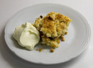 Sweet desserts. Apple crumble slice of cake with cream on a white dish in the kitchen table.	
