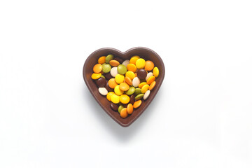 multi-colored sweet candies   in heart shaped bowl on white background, top view. Space for text