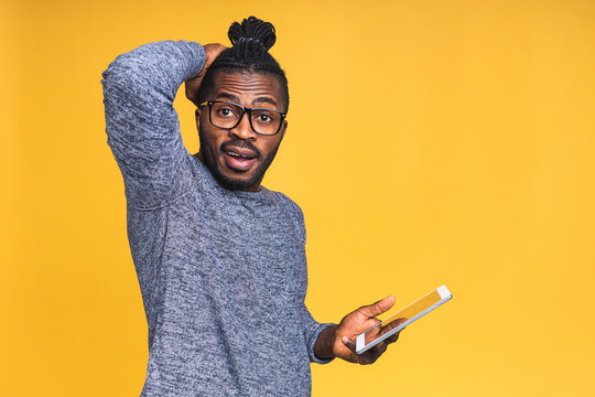 Working On Digital Tablet. Portrait Of Surprised Amazed Young African American Black Man Holding Digital Tablet While Standing Isolated Over Yellow Background.