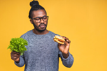 Hungry young african american black man eating hamburger isolated over yellow background. Holding lettuce. Diet concept.