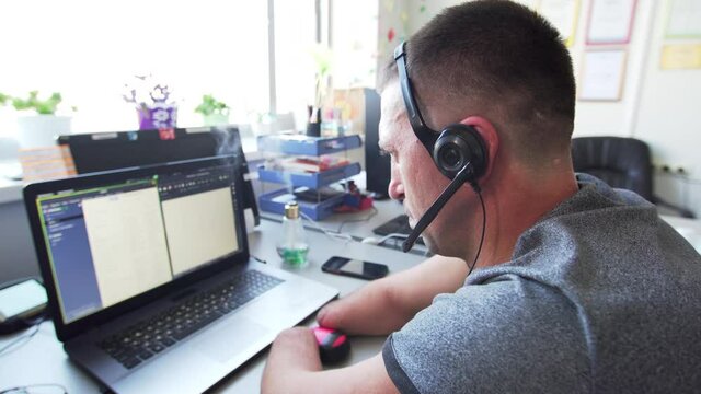 A caucasian man with amputated two stump hands and legs types at the laptop and uses a mouse. A man with a disability in earphones works in call-center at the laptop