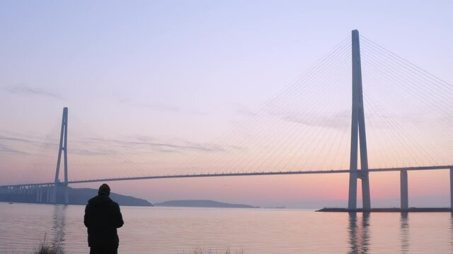 Flying backwards: silhouette of the cable-stayed Russian bridge across the Eastern Bosphorus strait at sunrise and a photographer taking pictures of it
