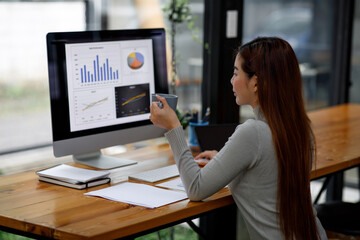 Smiling Young business woman working on a laptop computer in a modern office,doing finances, accounting analysis, report data pointing graph Freelance education and technology concept.