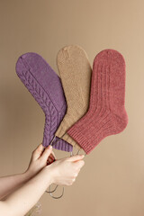 Three woolen socks in women hands on beige background