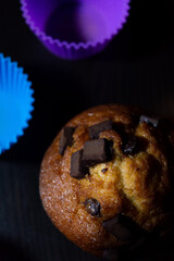 Banana Chocolate Chip Muffin on A Black Background with cupcake holders around the Muffin