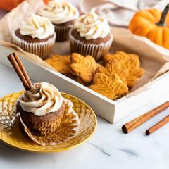 A tray of pumpkin spice cookies and cupcakes with one in front ready for eating.