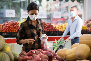 Asian woman wearing protective mask choosing fresh fruits and vegetables in grocery shop. Concept...