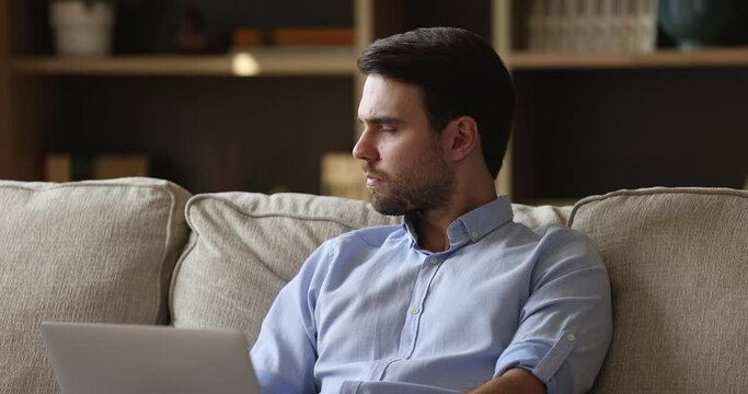 Millennial male software developer engaged in work from home at living room look on laptop screen write program code think on problem solution create new app. Pensive young man study online using pc