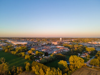aerial view of urban city in autumn with bright blue sky and colored foliage.  water tower seen in distance.  neighborhood marked by rows of trees. blue sky in horizon with pink tinges of sun.      
