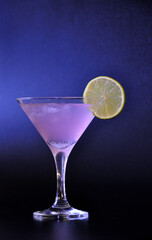Tall glass of Cosmopolitan cocktail with a slice of ripe lime on a black background.