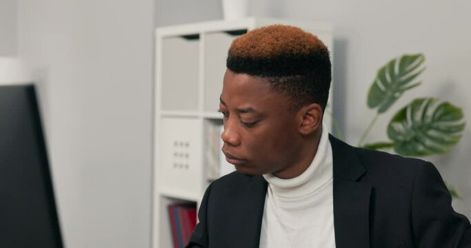 A close-up of face of dark-skinned man working in an office, law firm, boy is sitting behind desk in front of computer checking the correctness of documents, sorting reports, entering data into system