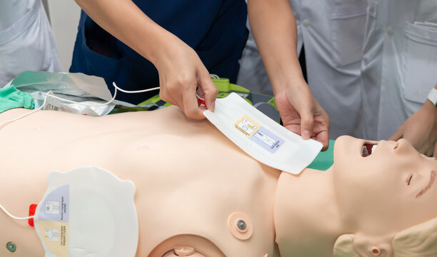 CPR training medical procedure workshop. Demonstrating chest compressions and use of AED automatic defibrillator on CPR doll.