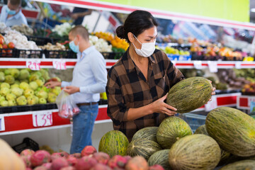 Asian woman wearing protective mask choosing fresh fruits and vegetables in grocery shop. Concept of shopping and social distancing in pandemic