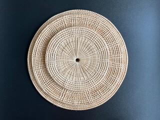 Round shape woven rattan placemat on black background, handmade kitchenware, weave craft product 