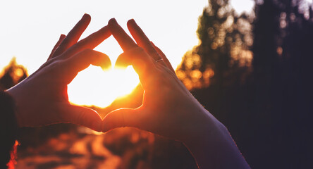 A woman shows a "heart" gesture with her hands at sunset. Heart-shaped hands