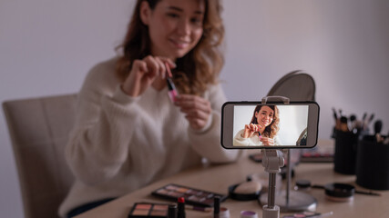 Young caucasian woman is recording an online make-up training video on her mobile. Video blogger girl applies makeup.