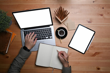 Young man using computer laptop and writing information on notebook.