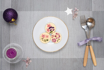 Christmas table decorations with a plate of edible flower biscuits and scented candle.  Flat lay Christmas decoration.