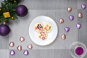 Obraz na płótnie Canvas Christmas table decorations with a plate of edible flower biscuits, chocolate candies and scented candle. Flat lay Christmas decoration.
