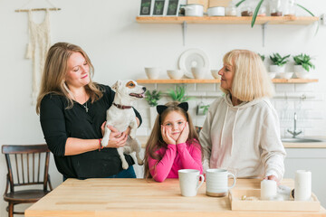 Happy granddaughter and grandmother and daughter having fun with jack russell terrier dog. Grandma hugs grandchild at home. Relationship, family and three generation concept.