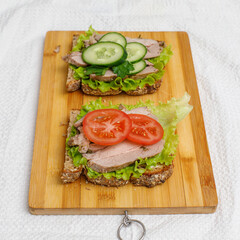 Fresh sandwiches with baked meat and vegetables on cutting board