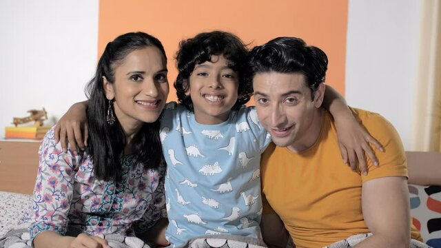 A young couple posing happily for pictures with their sweet and adorable child. Closeup shot of a small child hugging his parents while sitting with them on the bed at home - relationship and bonding