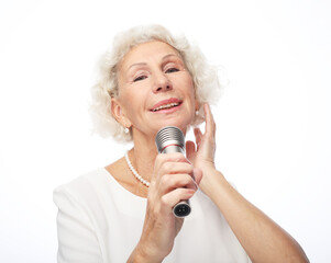 Happy old woman wearing white shirt holding a microphone and singing