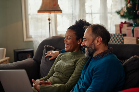 Diverse smiling couple using laptop at home