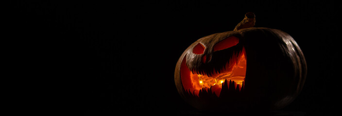 A creepy pumpkin with a carved grimace glows. Jack on a lantern in the dark.