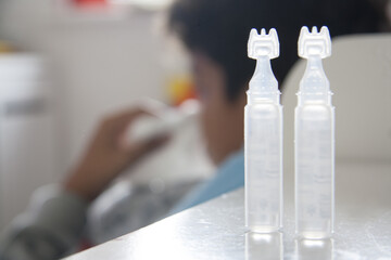 Transparent plastic bottle for nasal spray in the foreground. Saline water solution for treating nose congestion. Blurred child blows nose. Runny nose, cold, allergy. 