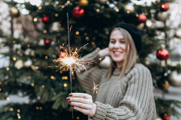 A burning Christmas fire in the hands of a modern woman on the background of a Christmas tree. Emotions, New Year mood. Winter holidays