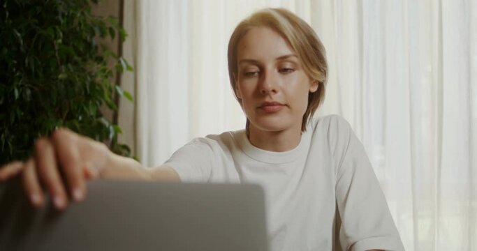 Young woman sits down at the breakfast table, opens a laptop and drinks coffee