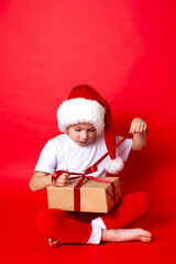 Merry Christmas. Portrait of a cute boy in a santa cap with gift boxes on a red background. A place for text.