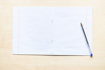 top view of pen and blank open school notebook with squared sheets with margins on light brown...