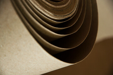 Fototapeta na wymiar kraft paper roll. curled beige material close up. cardboard production concept