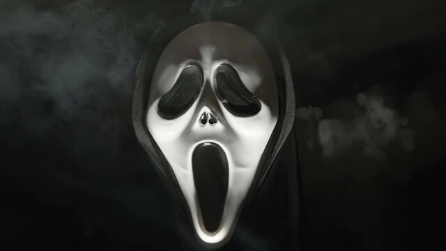 A ghost face in white mask with the black cloth and the smoke on the back during the halloween in Estonia